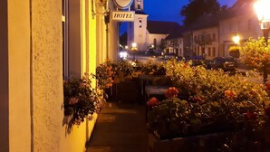 A hotel with a signboard, a bell tower, and flower arrangements along the sidewalk. - Hotel Krone (Lindow)