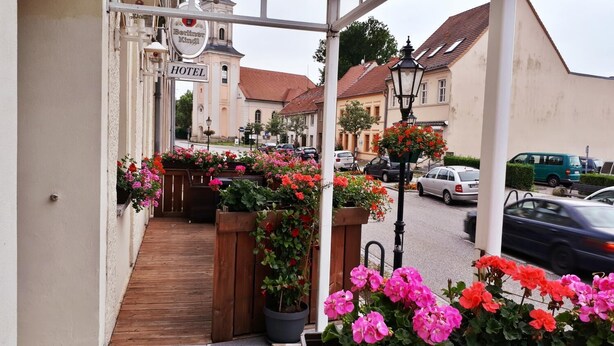 A hotel entrance with a wooden staircase leading to a covered area with flower planters. - Hotel Krone (Lindow)