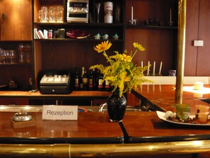 A reception area with a wooden counter, a vase with yellow flowers, a cash register, and a sign labeled "Reception". - Hotel Krone (Lindow)