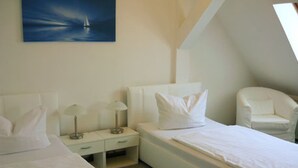 A hotel room with two beds, a nightstand, a chair, and a painting of a sailboat on the wall. - Hotel Krone (Lindow)