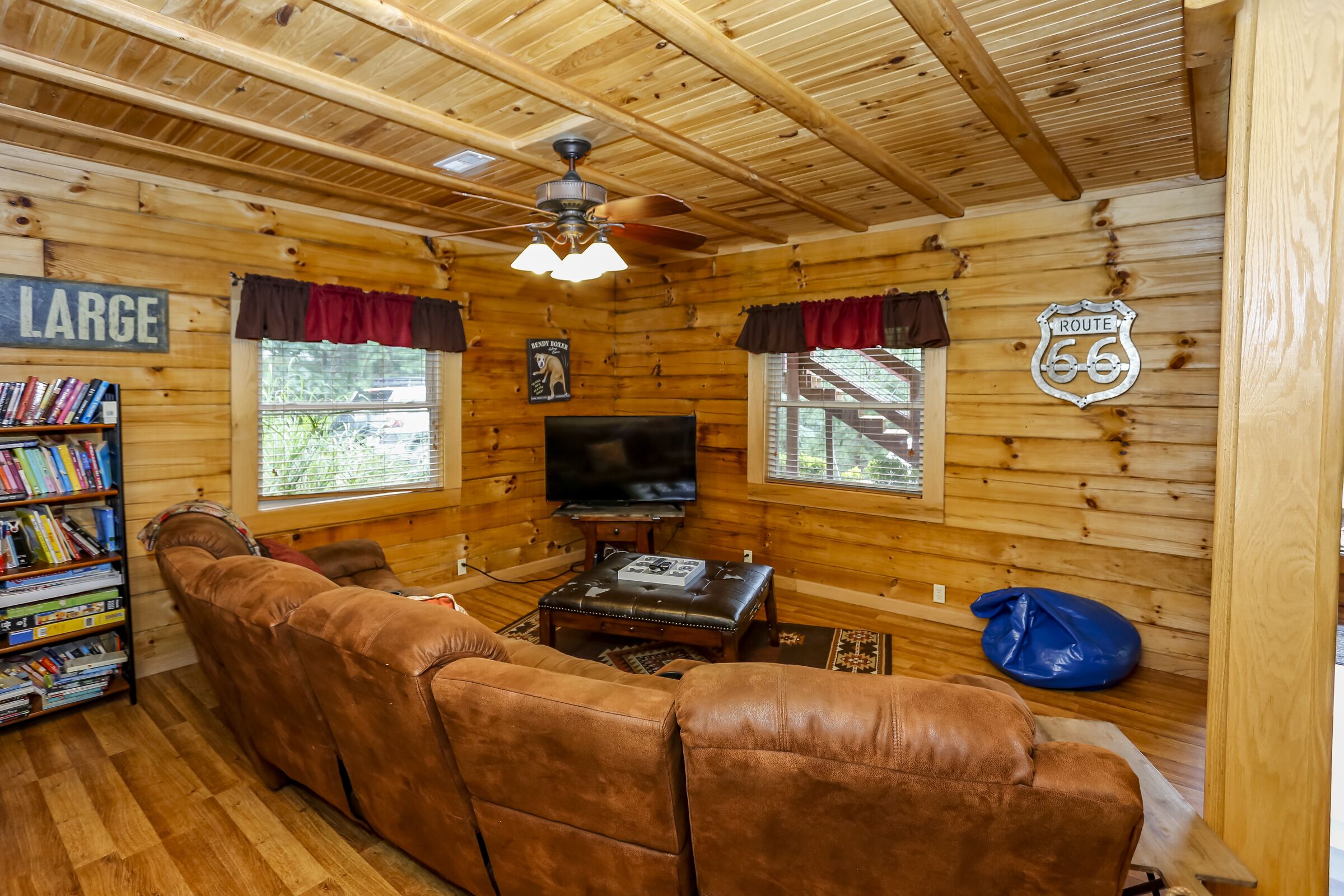 A cozy cabin interior with a large brown leather sofa, a television, and a bookshelf filled with books.