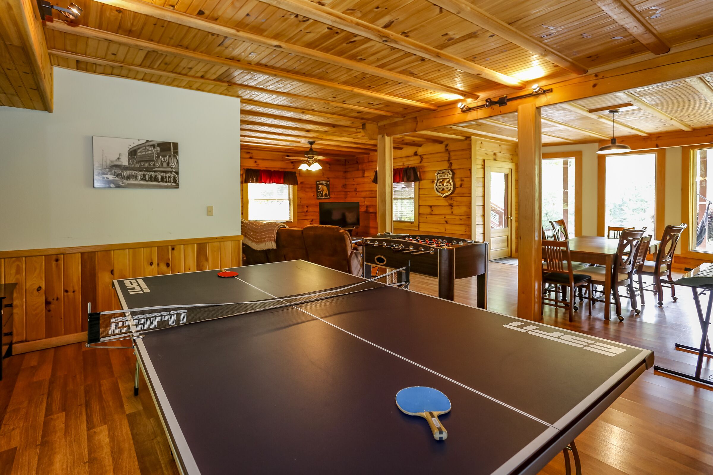 Ein Tischtennistisch mit blauem Schläger, ein Kicker und ein Essbereich mit Stühlen und Tisch.