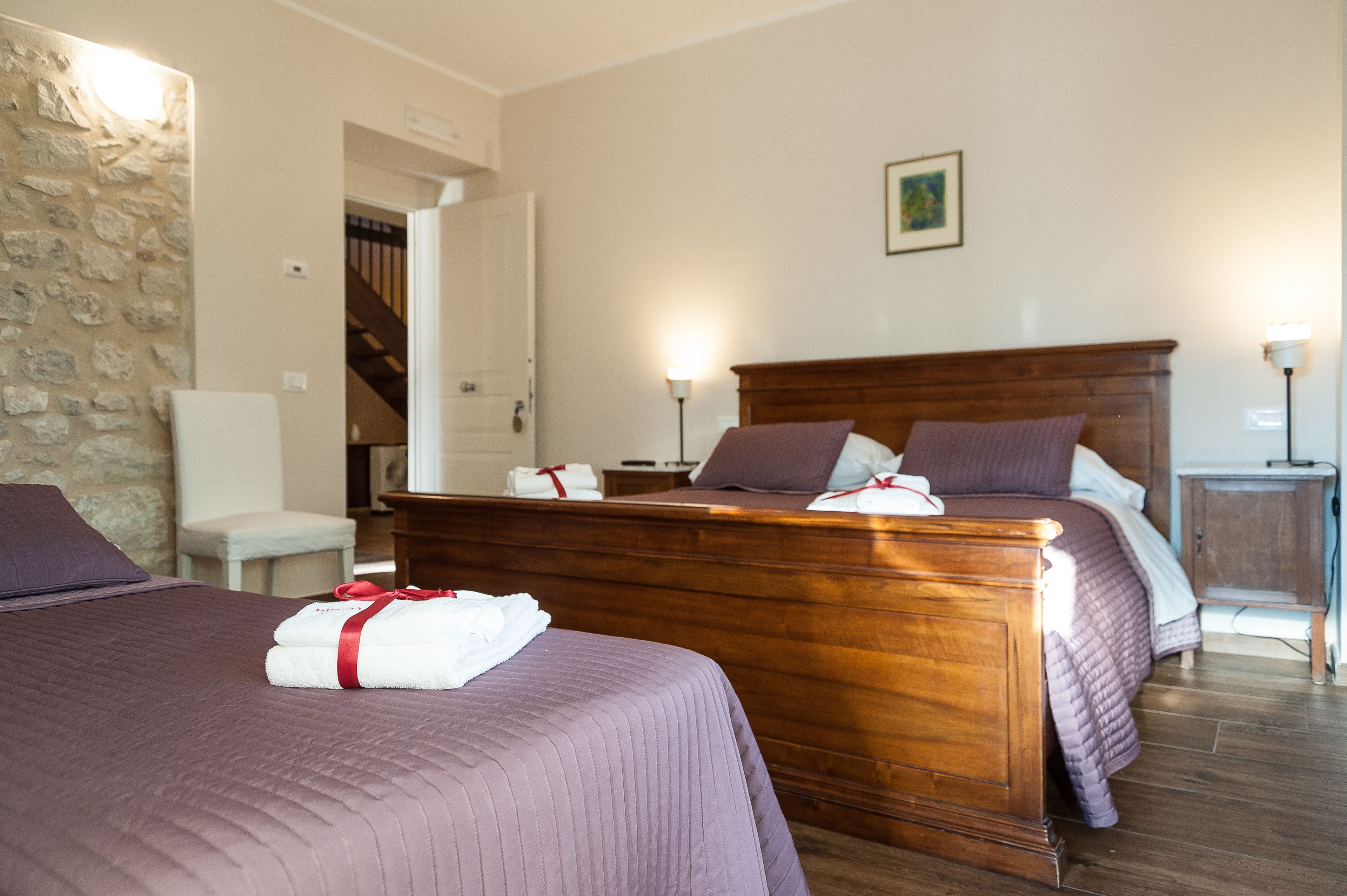 A hotel room with two beds, a wooden headboard, a stone wall, a chair, a nightstand, and a staircase.