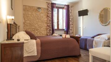 Une chambre avec un mur en pierre, un grand lit avec une tête de lit, une télévision et une fenêtre avec des rideaux.