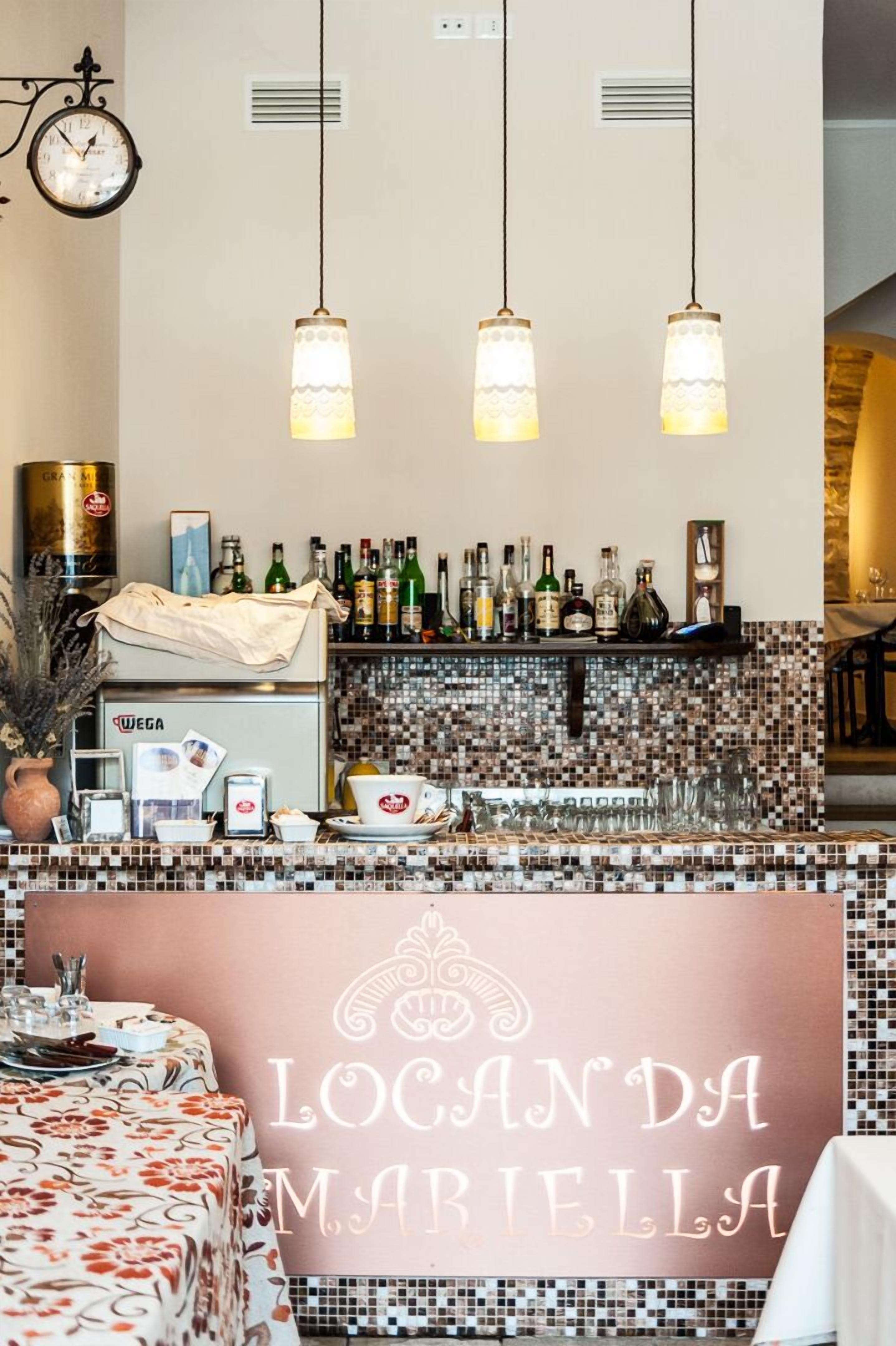 Angolo bar con schienale piastrellato, luci a sospensione e orologio a parete.