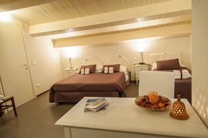 Habitación de hotel con dos camas, una mesita con una revista y una bandeja de frutas, y una mesita de noche con una lámpara.
