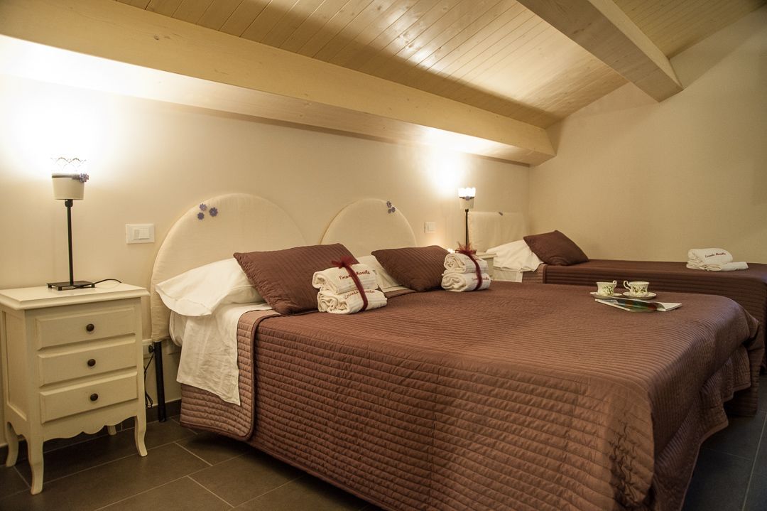 A hotel room with two beds, each with a brown quilted bedspread and pillows. There are bedside tables with lamps and a small drawer.