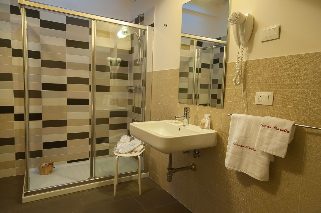 Un baño con ducha de mampara de vidrio, lavabo, secador de pelo y toallas con texto.