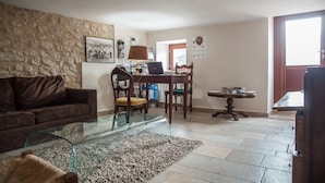 A living room with a glass coffee table, a brown sofa, a dining area with a wooden table and chairs, and a stone wall. - La Locanda di Mariella (Poggio Picenze)