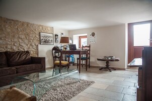 Una sala de estar con una mesa de centro de vidrio, un sofá marrón, un comedor con una mesa y sillas de madera, y una pared de piedra.