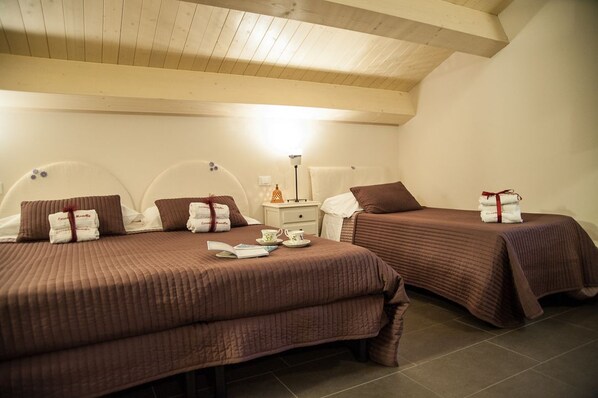 A hotel room with two beds, each with a brown bedspread and pillows, a nightstand with a lamp, and a small table with a teapot and cups.