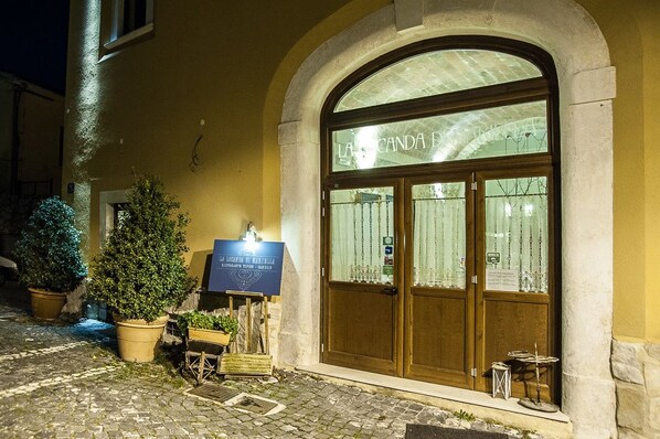 A building with a large arched entrance, a signboard, and potted plants outside. - La Locanda di Mariella (Poggio Picenze)