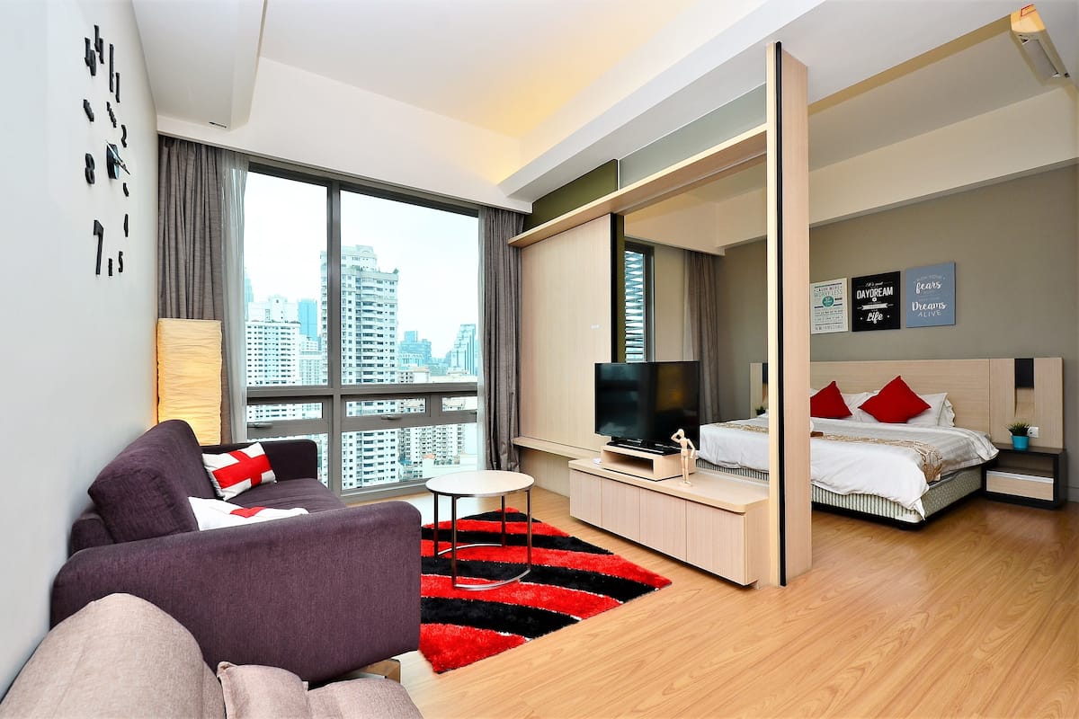 Une chambre d’hôtel moderne dotée d’une grande fenêtre, d’un canapé, d’un lit, d’une télévision et d’un bureau.