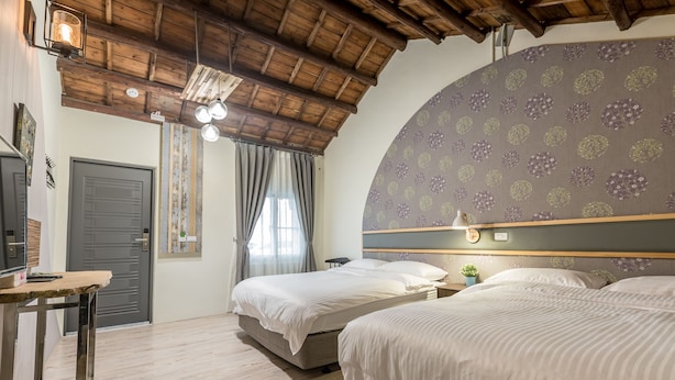 Una camera da letto con due letti, travi in legno a soffitto, un'ampia finestra con tende e una parete decorata con un motivo floreale.