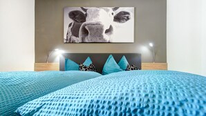 Quarto com cama, cabeceira e um quadro de vaca fixado na parede.