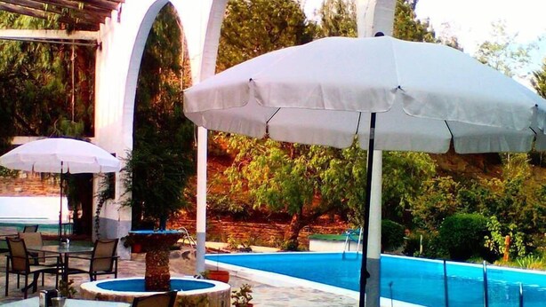 Un patio al aire libre con mesas, sillas, una piscina y sombrillas.