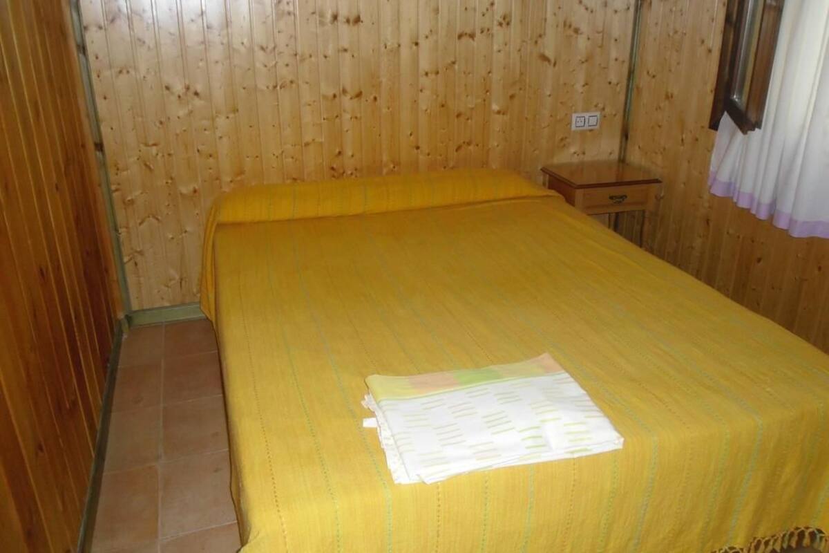 Un lit simple avec une couvre-lit jaune, dans une pièce aux murs en bois et au sol carrelé.