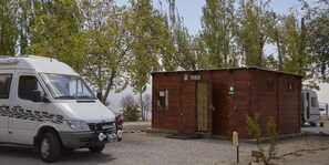 A white camper van parked next to a wooden cabin with a reception sign. - Camping Alpujarras (Nevada)