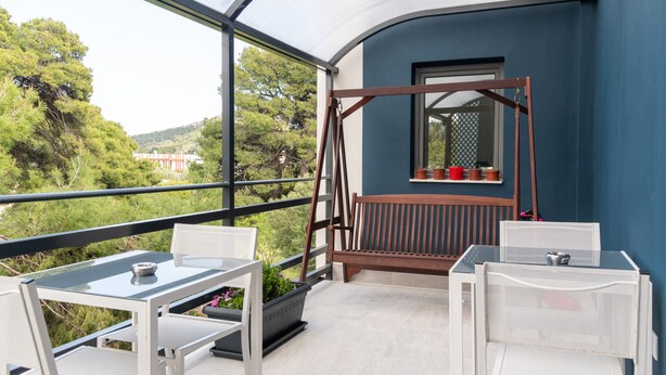 A balcony with a table and chairs, a wooden swing, and a view of greenery and buildings. - CHROMA Lodge Pikermi  (Rafina-Pikermi)