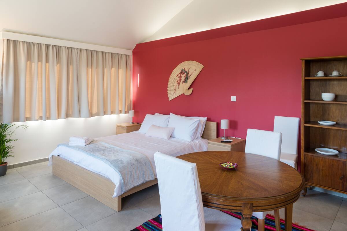 A modern bedroom with a bed, bedside tables, a round wooden table, and a decorative fan.