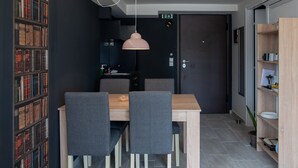 A modern dining area with a wooden table and grey upholstered chairs, a bookshelf filled with books, and a dark door in the background. - CHROMA Lodge Pikermi  (Rafina-Pikermi)