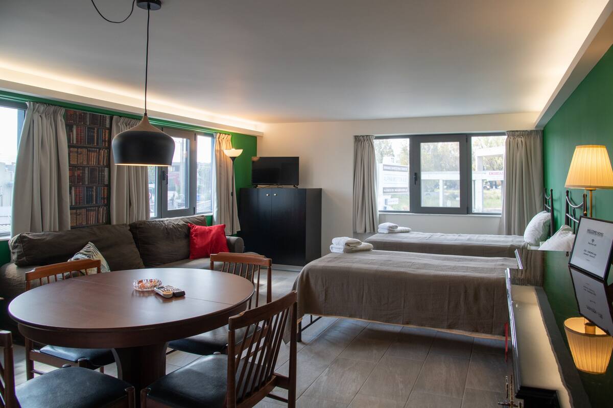 A hotel room with a sofa, two single beds, a dining table, and a TV.