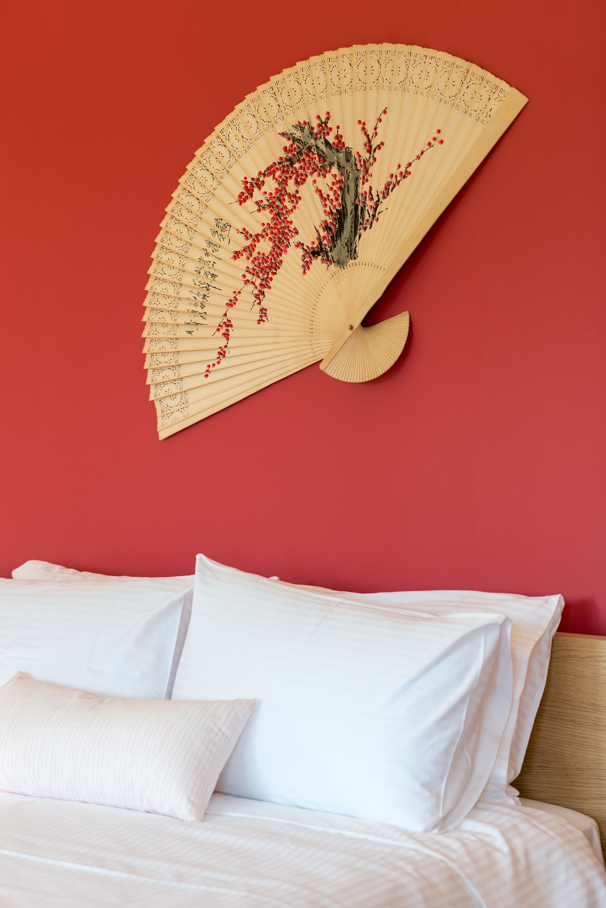 Una cama con sábanas y almohadas blancas, un tapiz beige con diseño floral y una pared roja.
