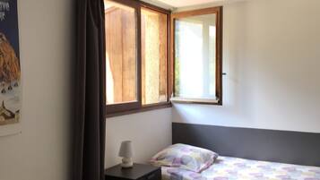 A room with two beds, a nightstand, a window with curtains, and a poster on the wall.