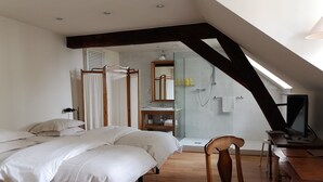 A bedroom with a bed, a wooden chair, a desk with a computer, a shower area, and a skylight. - B&B Het Leuvens Hof (Leuven)