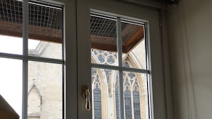 A window with a metal grid, a wooden door, and a view of a brick building with Gothic architecture. - B&B Het Leuvens Hof (Leuven)