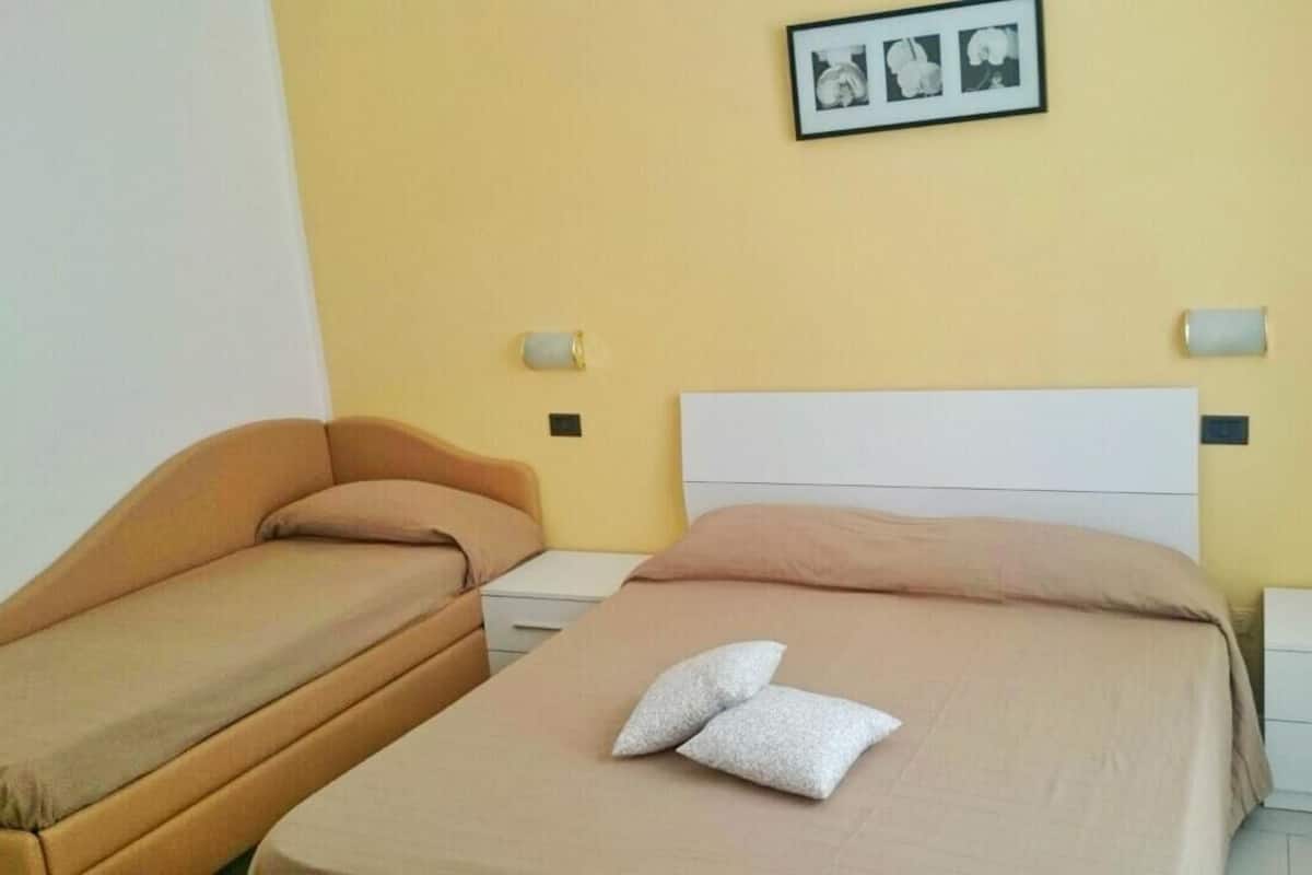 Quarto de hotel com duas camas, uma parede amarela e um quadro emoldurado acima das camas.