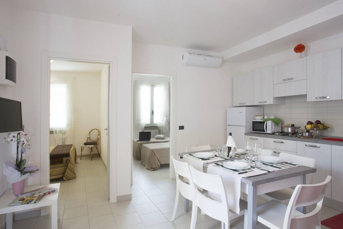Cozinha moderna com armários brancos, uma mesa de jantar posta para quatro e um pequeno espaço de refeições com uma cadeira.