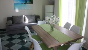 A dining area with a wooden table, green tablecloth, white chairs, and a vase with flowers. - Apartments Tanja & Josipa (Pag)