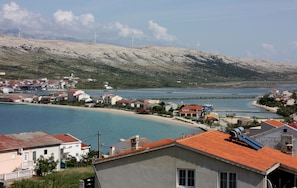 A coastal town with buildings along the shoreline, a body of water, and wind turbines in the background. - Apartments Tanja & Josipa (Pag)