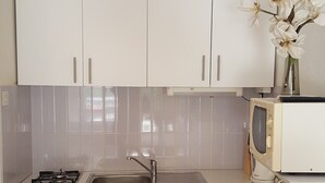 A compact kitchen with white cabinets, a stainless steel sink, a microwave, and a gas stove. - Apartments Tanja & Josipa (Pag)