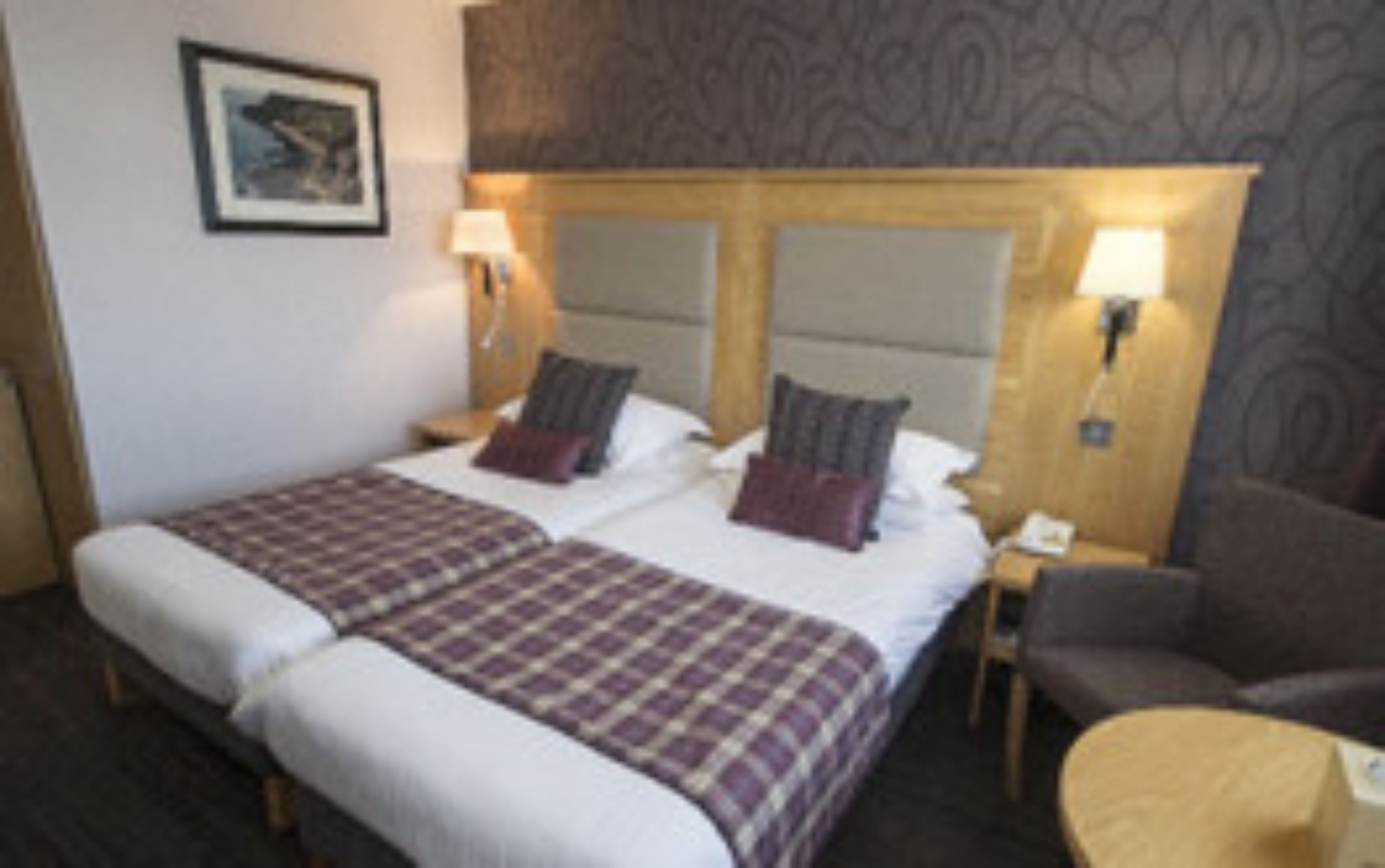 A hotel room with a large bed, two nightstands, a chair, and a small table.