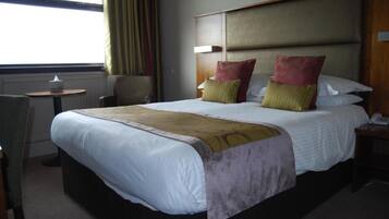 A hotel room with a large bed, a bedside table, a chair, and a window with curtains.
