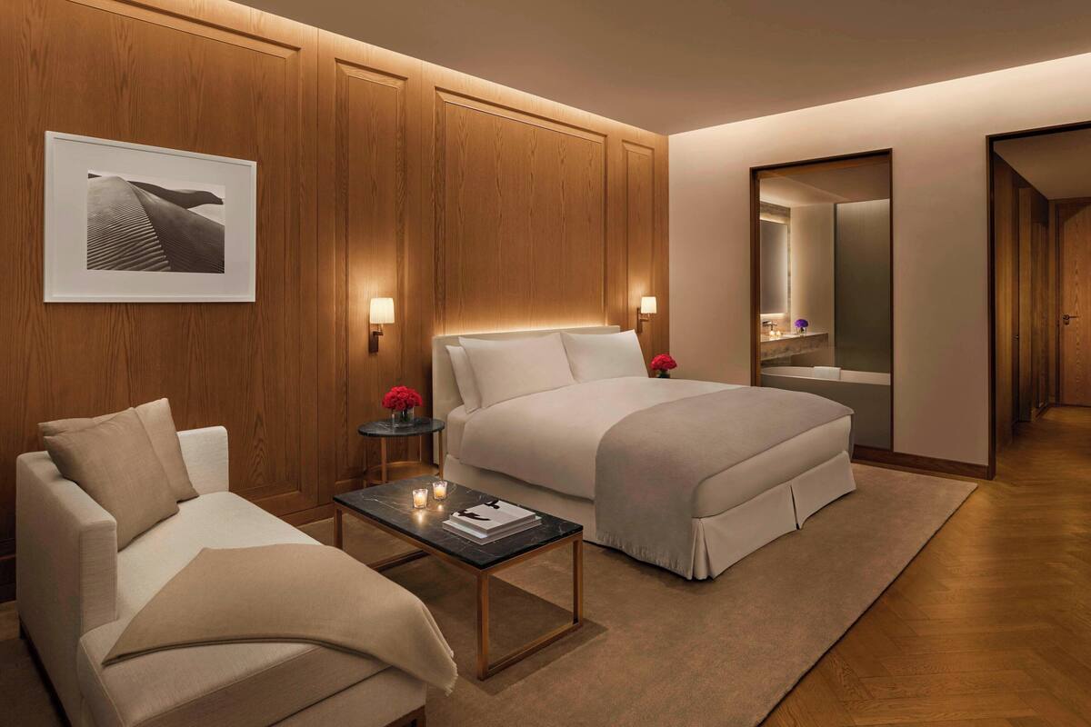 A modern hotel room with a large bed, a sofa, a small table with a book and a candle, and a framed picture on the wall.
