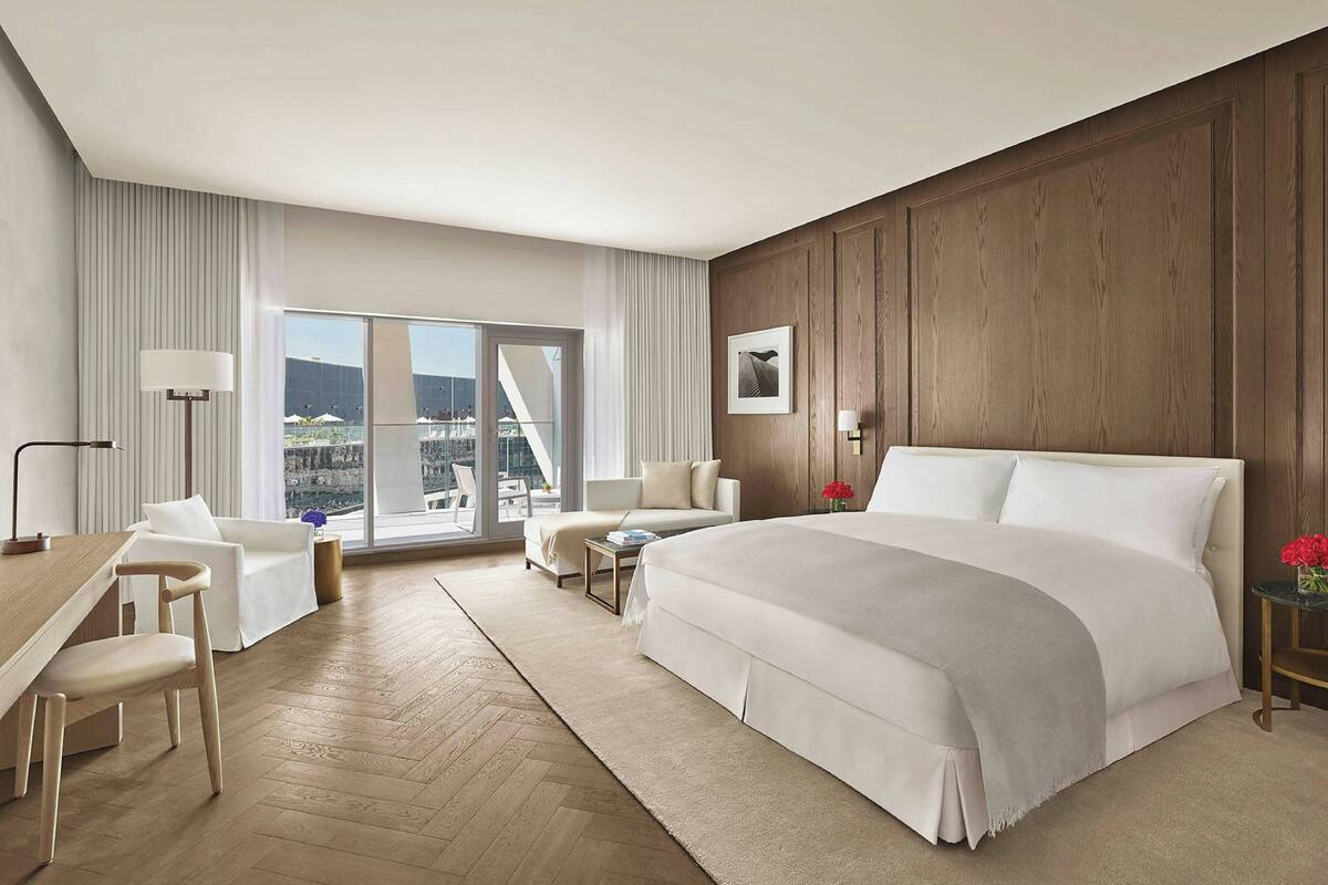 A hotel room with a large bed, a desk, a chair, a sofa, a small table, and a view of the city.