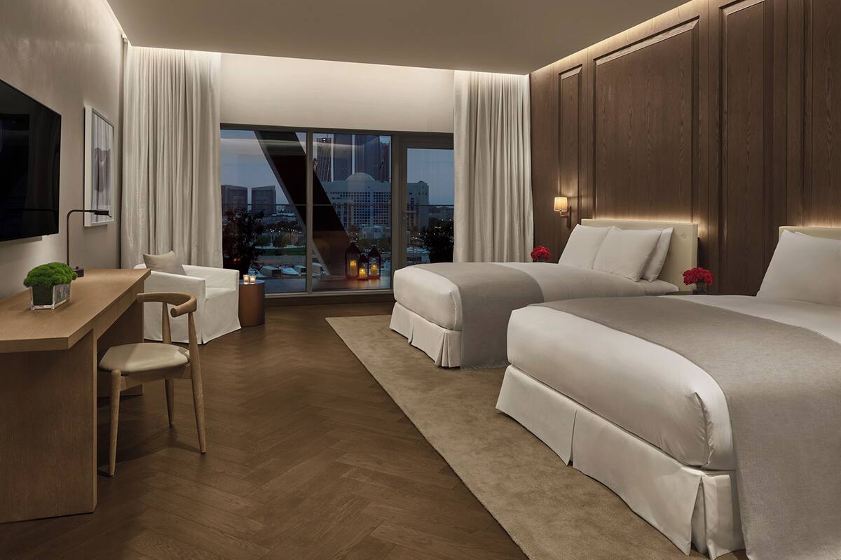 A hotel room with a large window, a desk, two beds, and a TV.