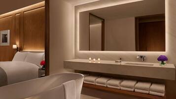 A modern bathroom with a large mirror, a bathtub, and a vanity with a sink and towel rack.