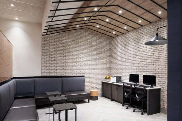 Un espace de bureau moderne avec un mur en briques, un canapé, un bureau doté de deux écrans et un luminaire suspendu.
