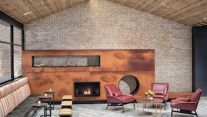 Un área de estar moderna con pared de ladrillo, chimenea, asientos de cuero y una mesa redonda con flores.