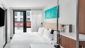 Habitación de hotel con una cama grande, una mesita de noche, un televisor y vistas al balcón exterior.