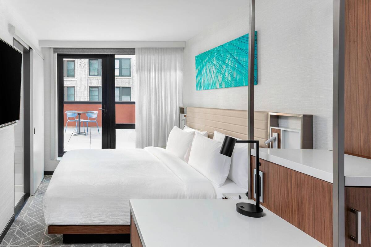 Une chambre d’hôtel avec un grand lit, une table de chevet, une télévision et une vue sur le balcon extérieur.