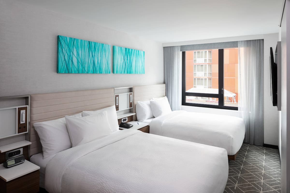 Une chambre d’hôtel avec deux lits, une grande fenêtre avec des rideaux et des œuvres d’art accrochées au mur.