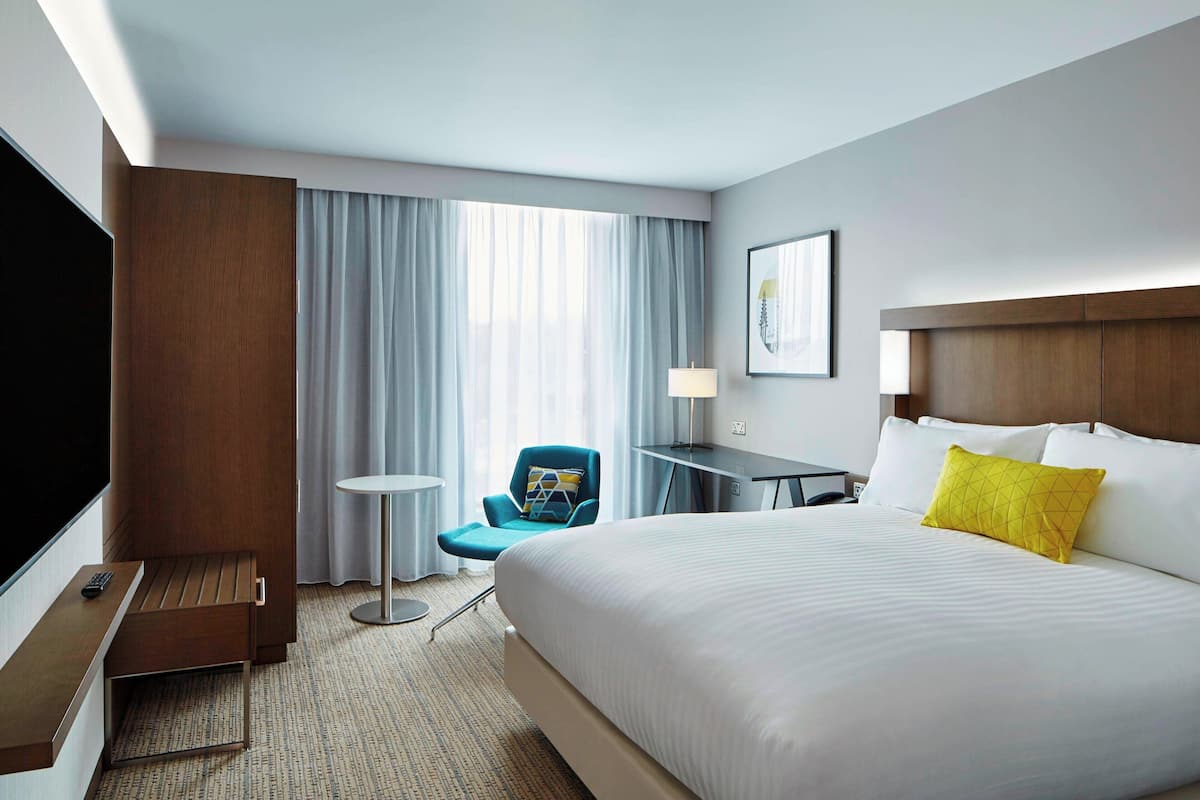 Habitación de hotel con una cama grande, un escritorio, una silla, un televisor y una ventana con cortinas.