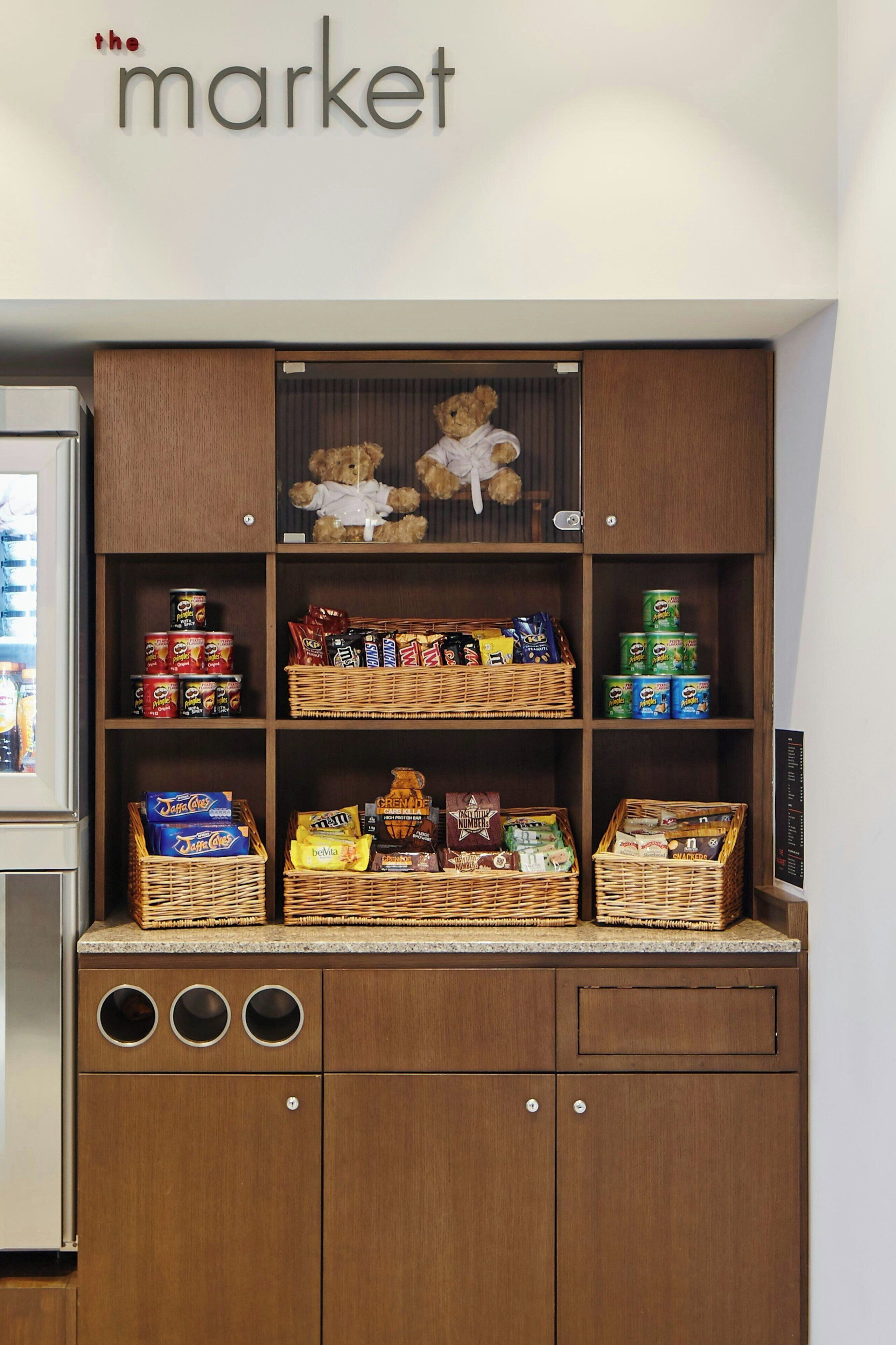 A wooden cabinet with shelves containing snacks, a teddy bear, and a sign reading "the market".