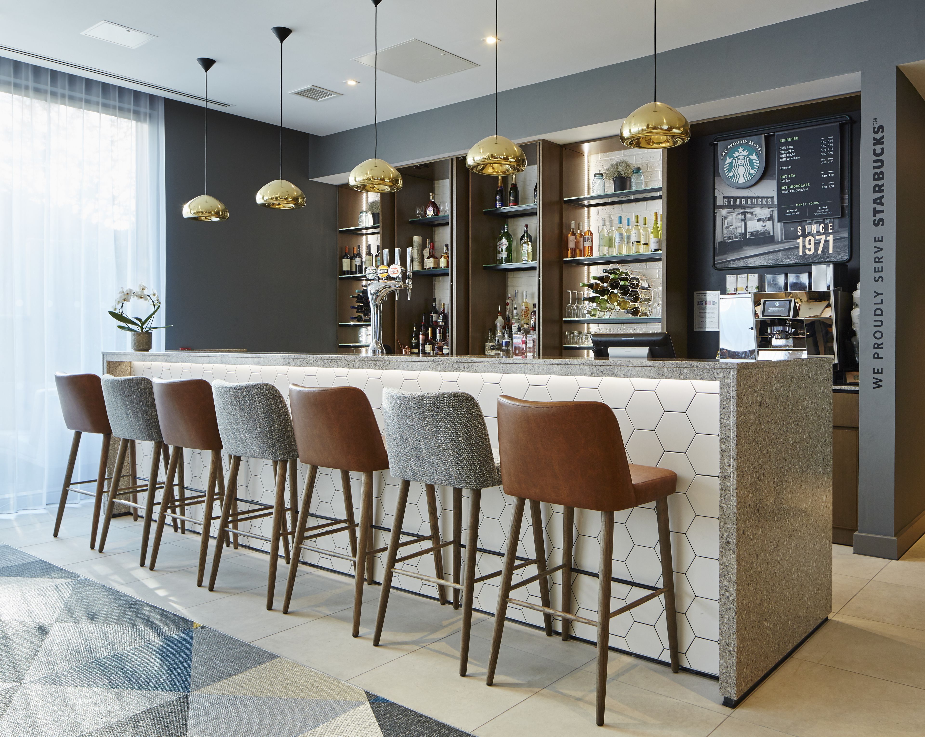 A modern bar area with a hexagonal tiled backsplash, a central bar counter, and four bar stools.