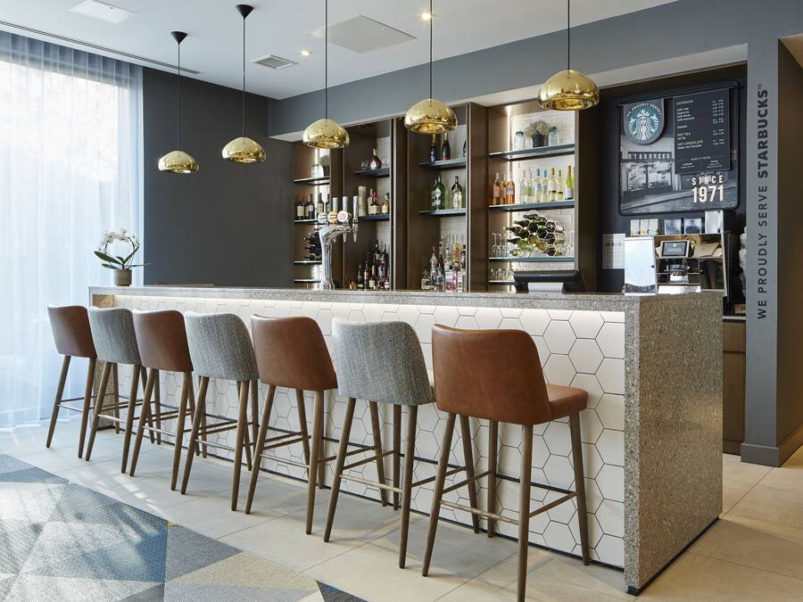 A modern bar area with a hexagonal tiled backsplash, a central bar counter, and four bar stools.